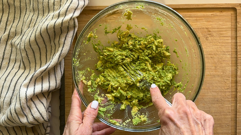 hand mashing avocado in bowl