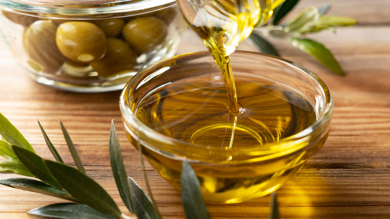 Olive oil poured in bowl whole olives wood