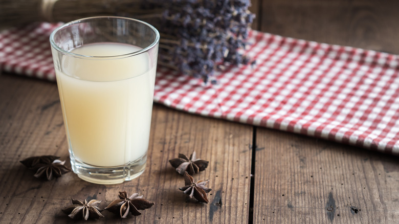 A glass of water and pastis on wooden table with checked fabric