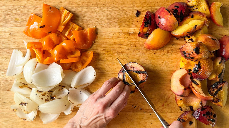 Cutting grilled bell pepper, onion, and peaches on cutting board