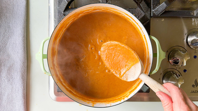 Peach bbq sauce simmering in pot on stove with wooden spoon