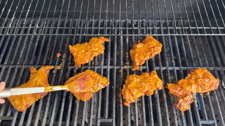 Brushing peach bbq sauce on chicken thighs on grill