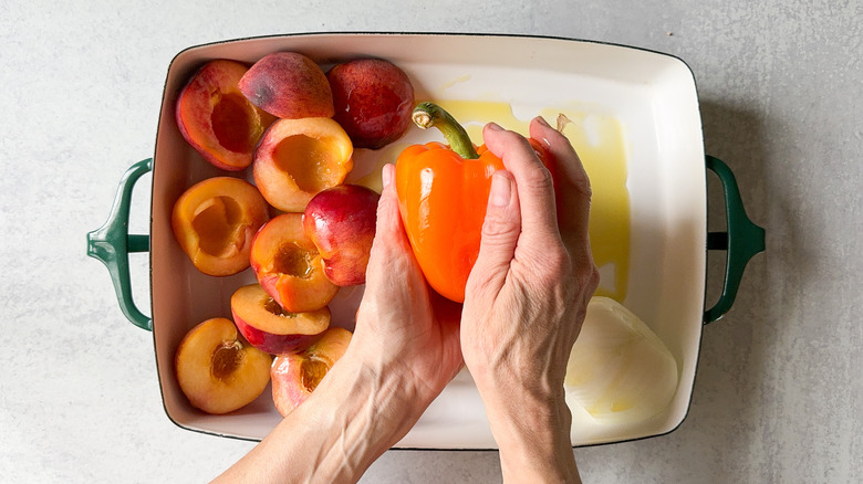 Rubbing peaches, peppers and onion with olive oil in baking dish