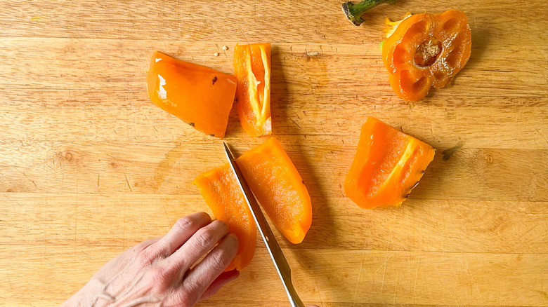 Cutting grilled orange bell pepper on cutting board