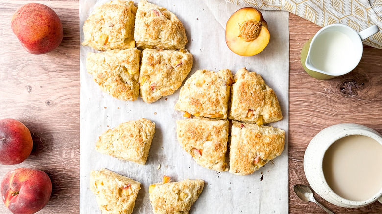 Peaches and Cream Scones on parchment paper on table top with peaches, cream, and tea