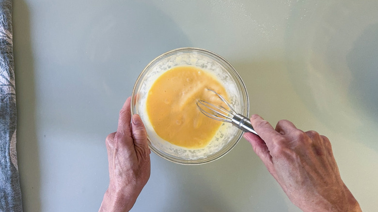 Whisking together eggs and heavy cream in glass bowl with whisk