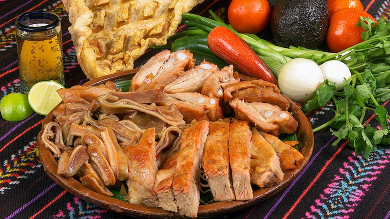 carnitas on a plate surrounded by vegetables and lime