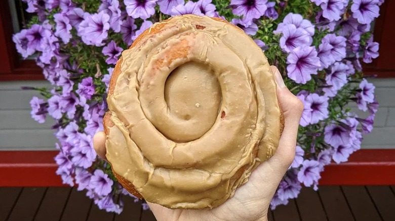 Hand holding a Persian donut in front of purple flowers