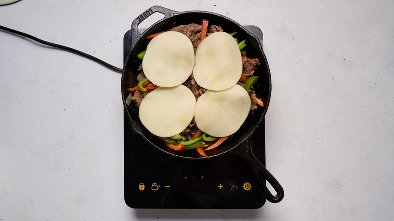 melting cheese over peppers and steak in skillet