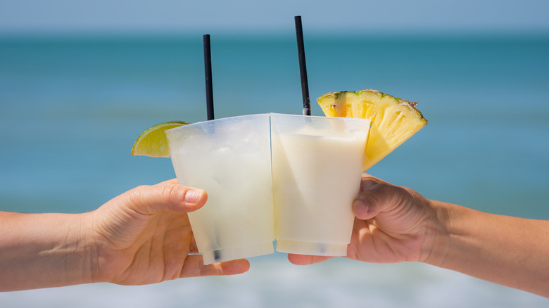 Hands clinking pina coladas on beach