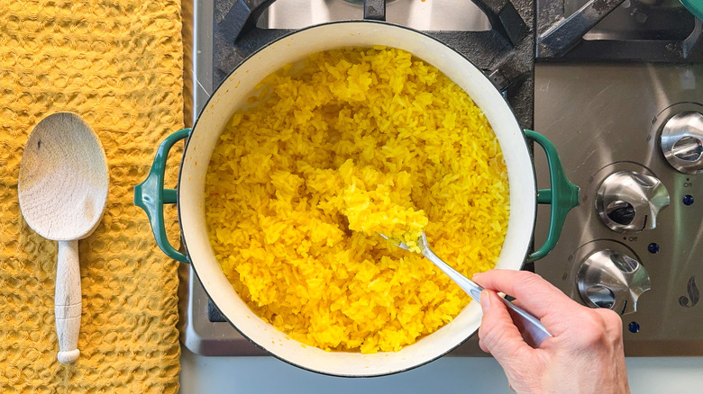 Fluffing saffron rice with fork in pot on stove top