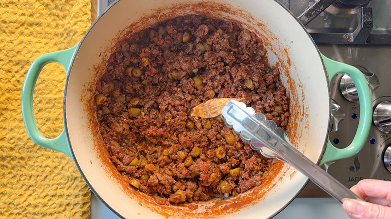 Removing bay leaf from Cuban picadillo in pot on stove top