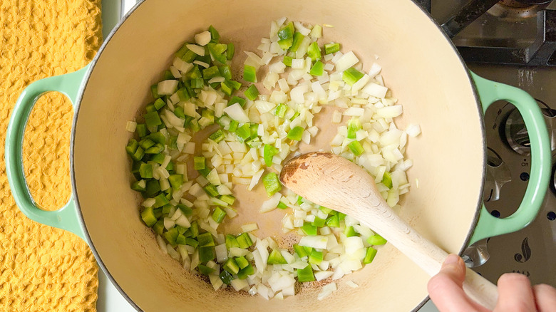 Diced green bell pepper and onion in large pot with wooden spoon