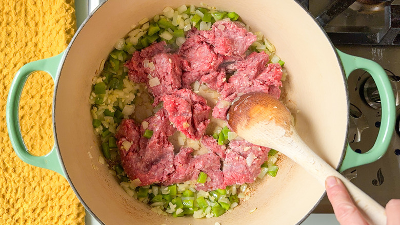 Stirring ground beef, garlic, onion, and green bell pepper in large pot on stove top