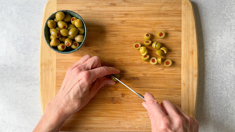 Slicing pimento-stuffed Spanish olives on cutting board