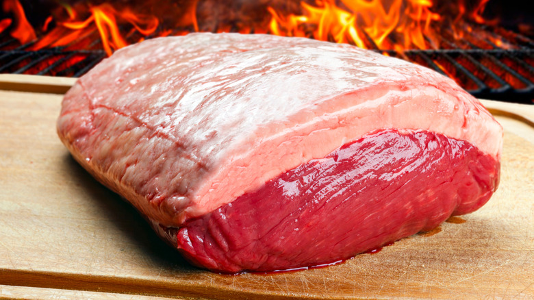 raw picanha on cutting board in front of grill