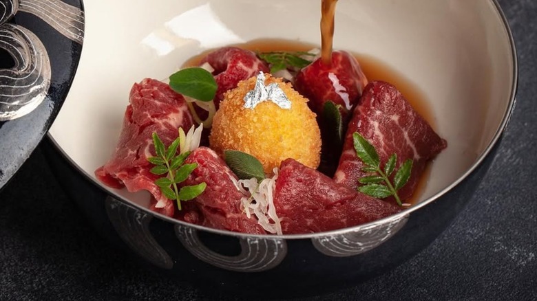 Breaded pigeon egg with sauce and meat in a bowl