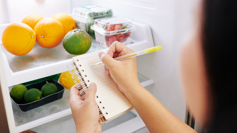 person checking refrigerator with list