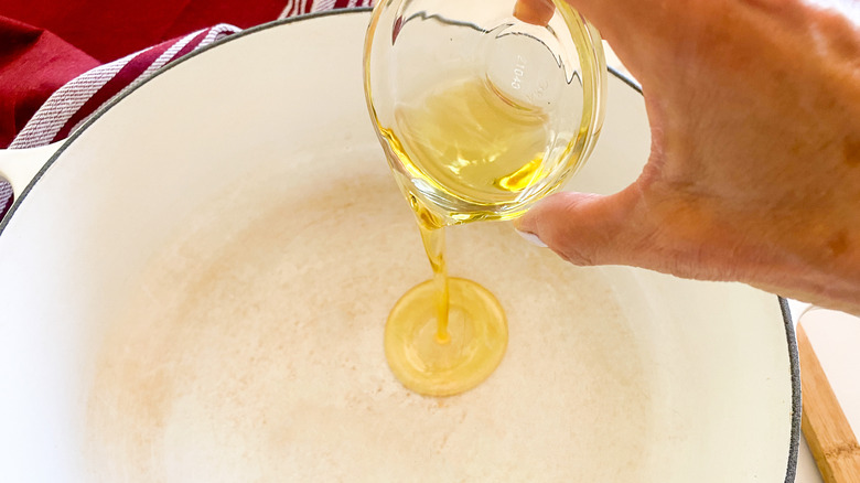 Hand pouring oil into soup pot