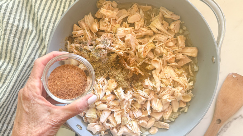 hand adding sugar to pan