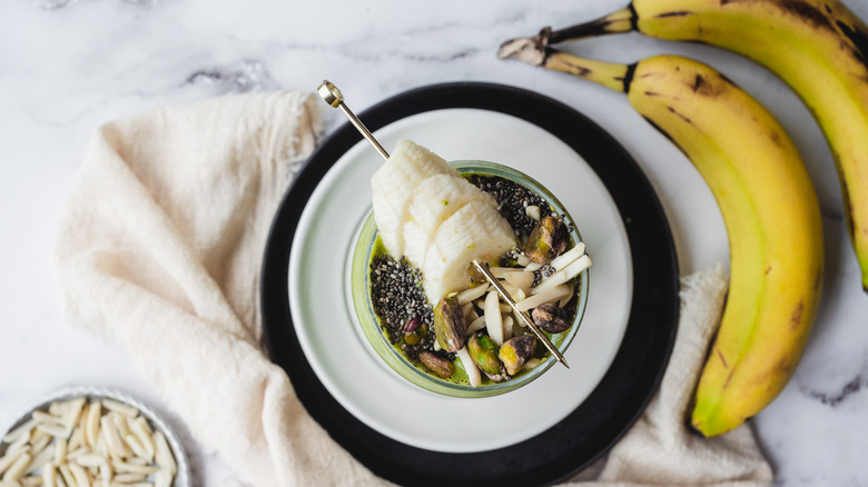 Green smoothie on white plate with bananas and almonds