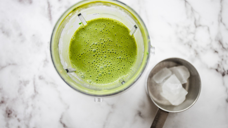 Green smoothie in blender with ice besides it