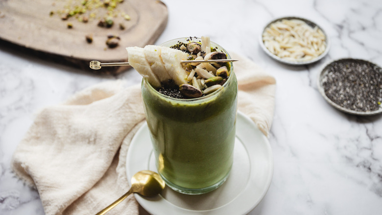 Green smoothie on white plate with pistachios, chia and almonds in background