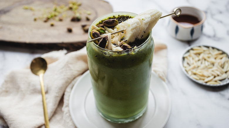 Green smoothie on white plate with pistachios and almonds in background