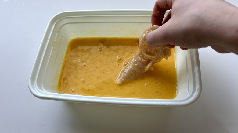 hand dipping chicken in egg