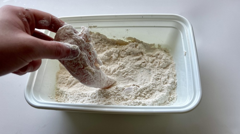 hand dipping chicken in flour