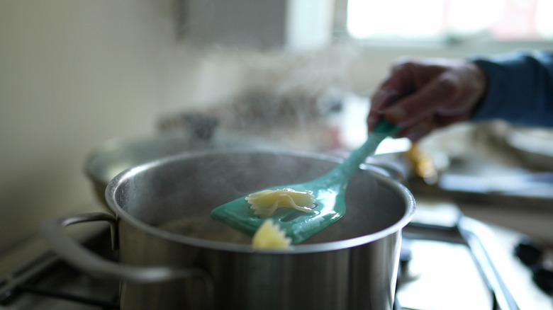 Hand holds spatula with noodle over pot