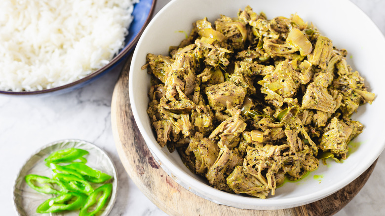 Bowl of jackfruit curry besides rice and green chili slices