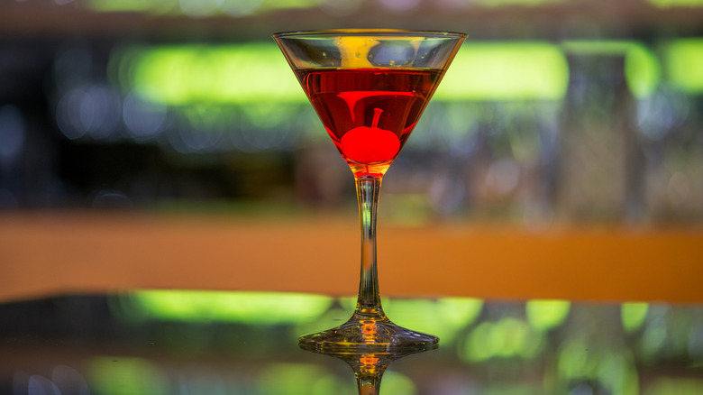 A red Manhattan cocktail on a bar table with a blurred background