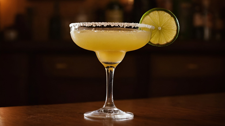 A margarita in a coupe with a salted rim and lime wheel