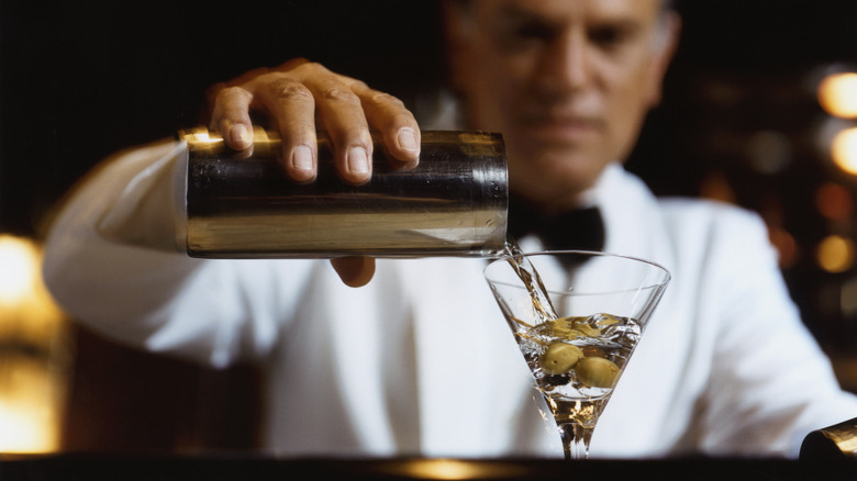 Bartender pouring a martini into a glass with olives