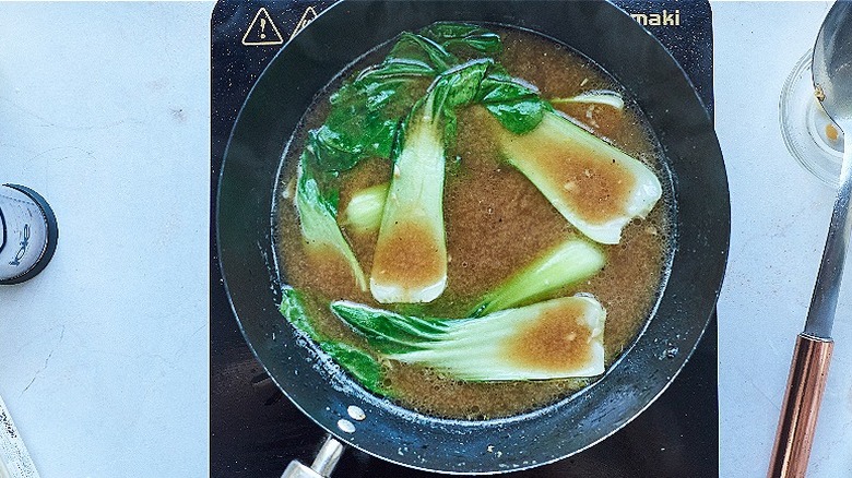 broth cooking in a wok with bok choy