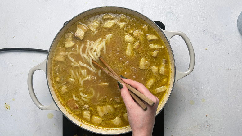 stirring japanese pork curry udon in pot with chopsticks