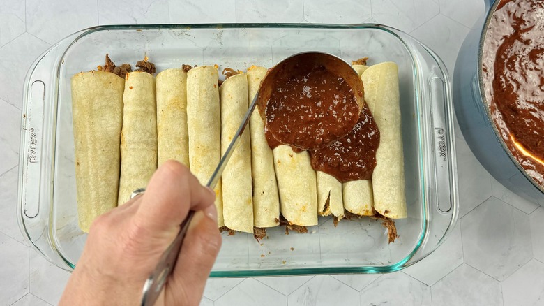 hand putting sauce on enchiladas