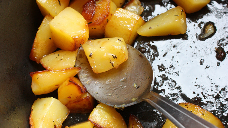 closeup of sauteed potato cubes and a metal spoon in a skillet