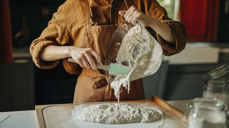 Baker scraping bread dough from bowl