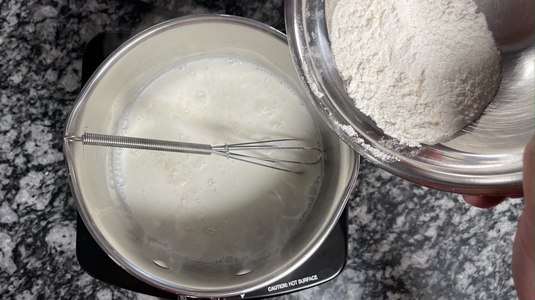 hand pouring flour into milk