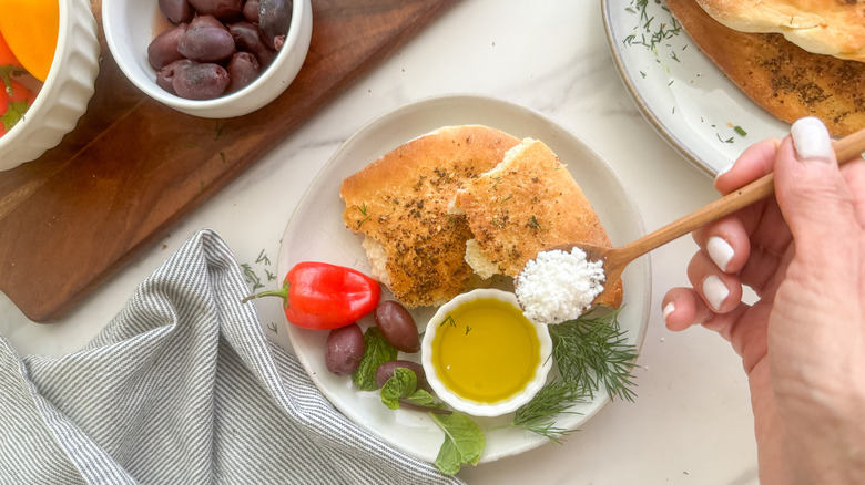 Hand spooning feta onto a plate of maneesh