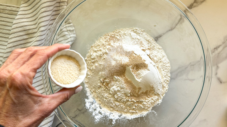 Hand adding sugar to a bowl of flour