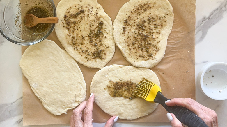 Hand brushing on za'atar paste to unbaked bread