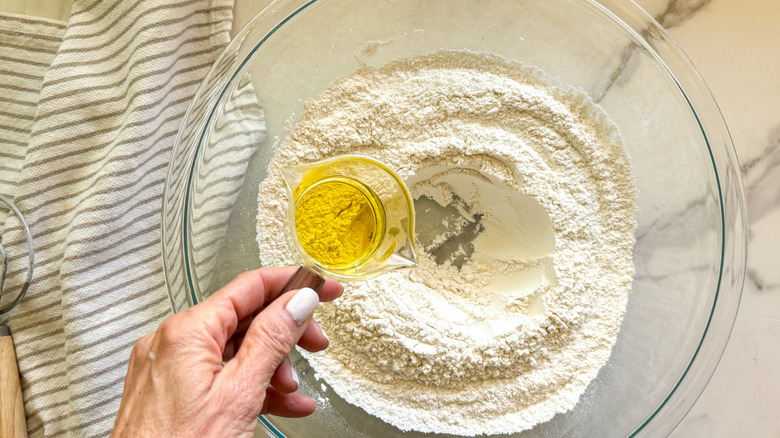 hand adding oil to a bowl of flour