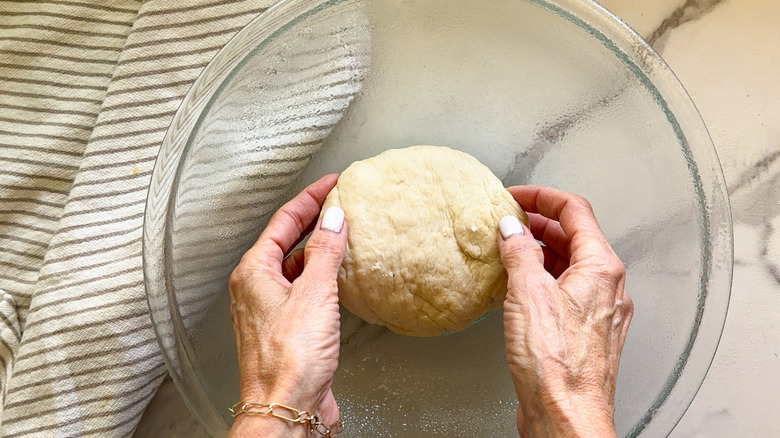 Hands placing dough in a glass bowl