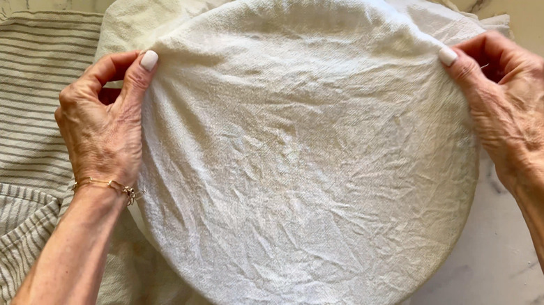 Hands covering bowl with a white towel