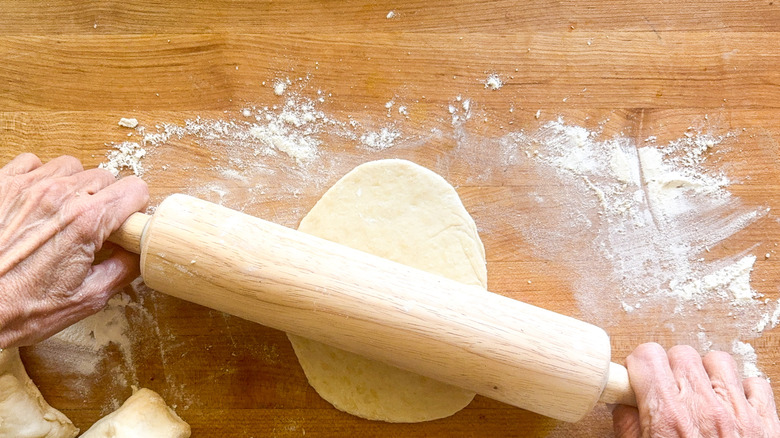 Hands rolling out dough with a rolling pin