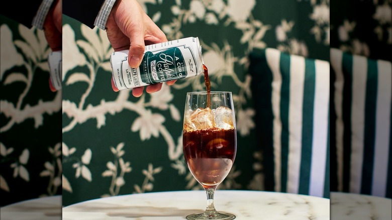 Hand pouring a can of Ralph's cold brew into a glass with ice