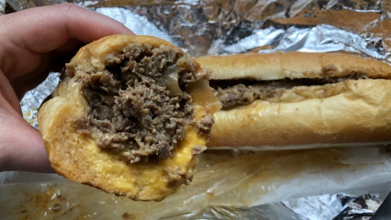 A hand holding half of a cheesesteak from Cosmi's Deli in south philly